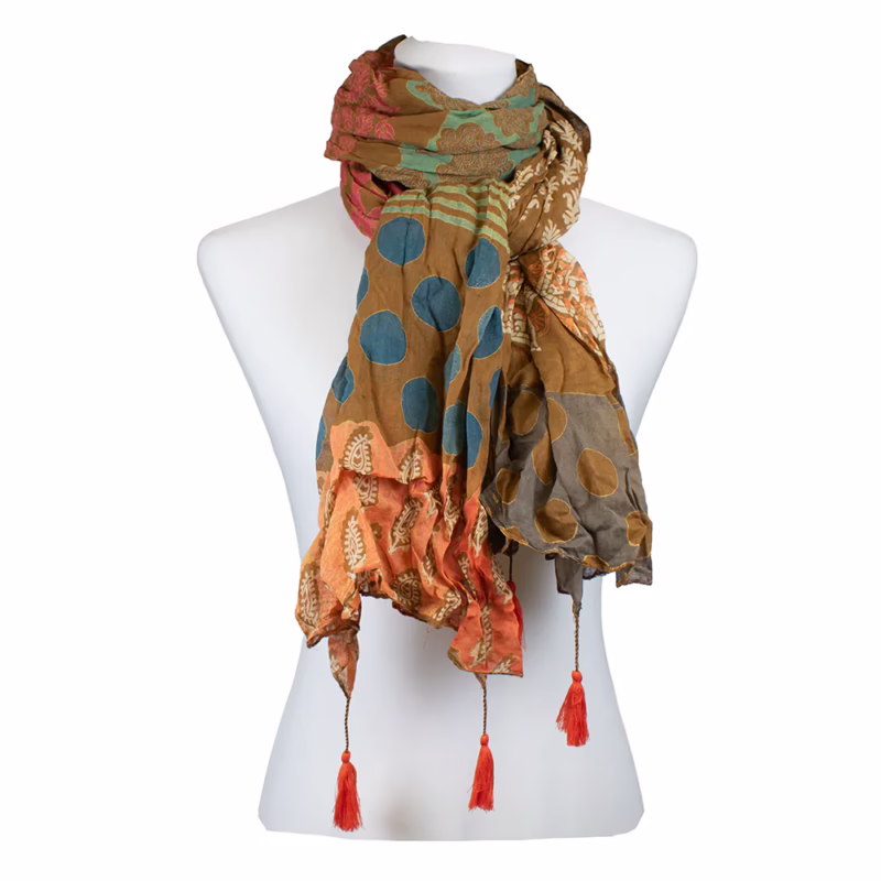 Mehrfarbiger Schal mit klar gegliederten Musterflächen. Kombination aus großen Punktmotiven in Blau auf orangefarbenem Grund, feinen Streifen in Grün und Gelb sowie ornamentalen Reihen in Creme. Farbverläufe zwischen Rost, Oliv und Orange entlang der Länge sichtbar. Abschlüsse mit sichtbaren Quasten in Orange.