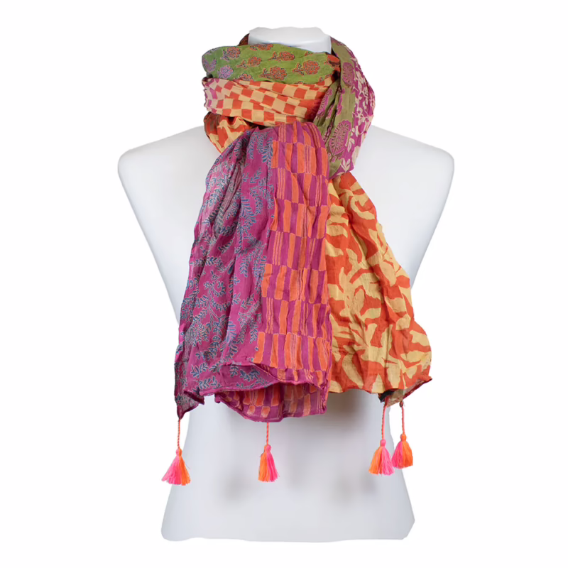 Mehrfarbiger Schal mit deutlich gegliederten Musterflächen. Kombination aus floralen Ornamenten, grafischen Linien und unregelmäßigen Flächen in Pink, Magenta, Grün und Türkis. Wechsel zwischen dichten Mustern und ruhigeren Farbpartien entlang der Länge. Abschlüsse mit sichtbaren Quasten in Orange und Pink.