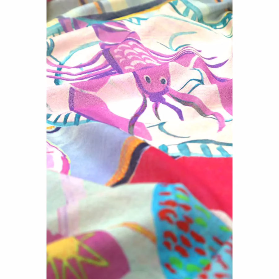 Detailaufnahme.Leichter Baumwollschal mit farbenfrohem Muster aus Fischen, Muscheln und abstrakten Detailaufnahme. Formen in Pink, Grün, Gelb und Blau, weich fallend.